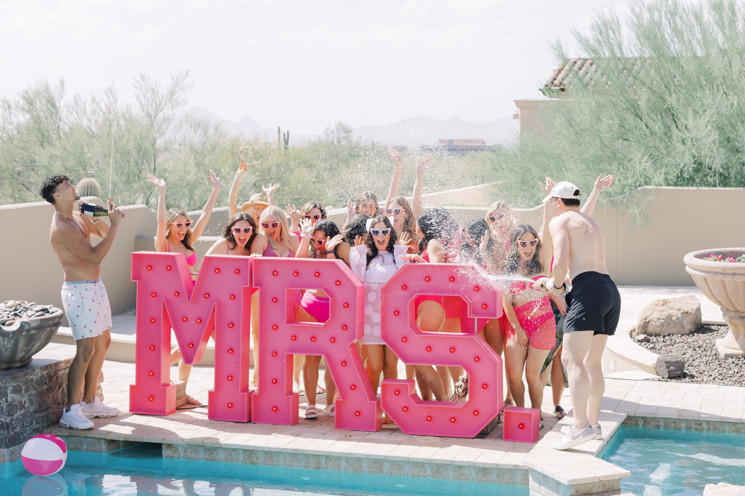 Bachelorette group celebrating in Scottsdale with a Barbie bachelorette theme, champagne squirt guns, pool boys, and giant MRS. marquee letters